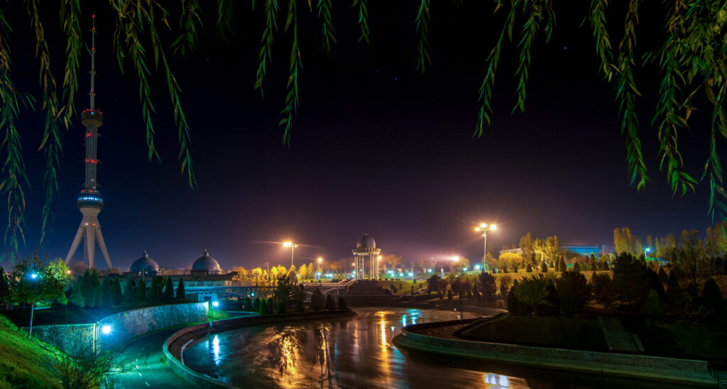A serene river at night, reflecting a vibrant Tashkent skyline illuminated against the dark sky